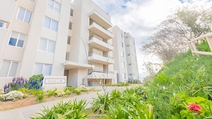 Un edifici residencial de diverses plantes amb balcons, un jardí paisatjístic i un cartell amb text.