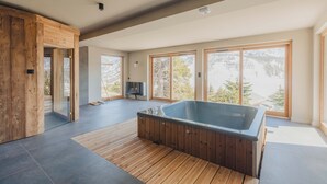 A modern interior with a wooden floor, a hot tub, and large windows offering a view of trees and mountains. - Chalet La Belle Etoile (Montgenèvre)