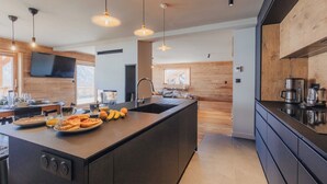 A modern kitchen with a central island, wooden accents, and contemporary lighting fixtures. - Chalet La Belle Etoile (Montgenèvre)