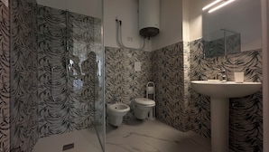 A bathroom with a toilet, bidet, and sink, all with a leaf-patterned wallpaper. - Puglia Promenade Apartment 5 (Bari)
