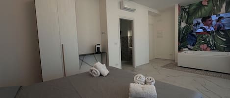 A hotel room with a bed, a bathroom, and a TV displaying a movie scene.