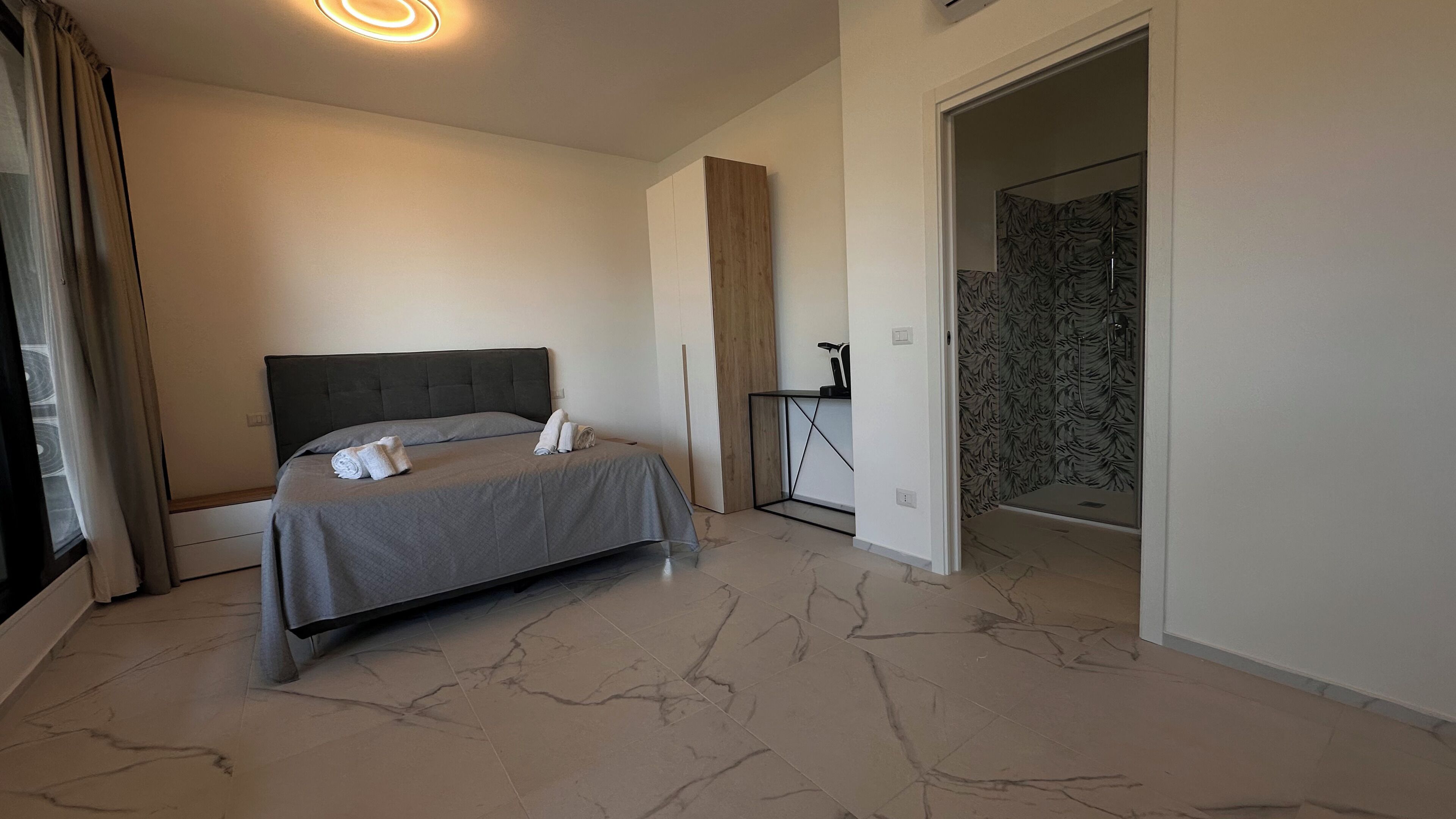 Une chambre à coucher moderne avec un grand lit, une table de chevet et un espace douche agrémenté d’un mur à motifs.