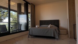 A modern bedroom with a large bed, a nightstand, and a chair by a balcony with a view of trees and a bridge. - Puglia Promenade Apartment 5 (Bari)