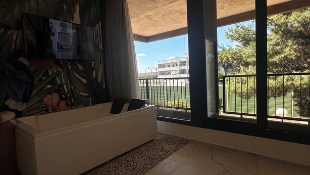 A spacious room with a large window, a white sofa, and a view of a basketball court. - Puglia Promenade Apartment 5 (Bari)