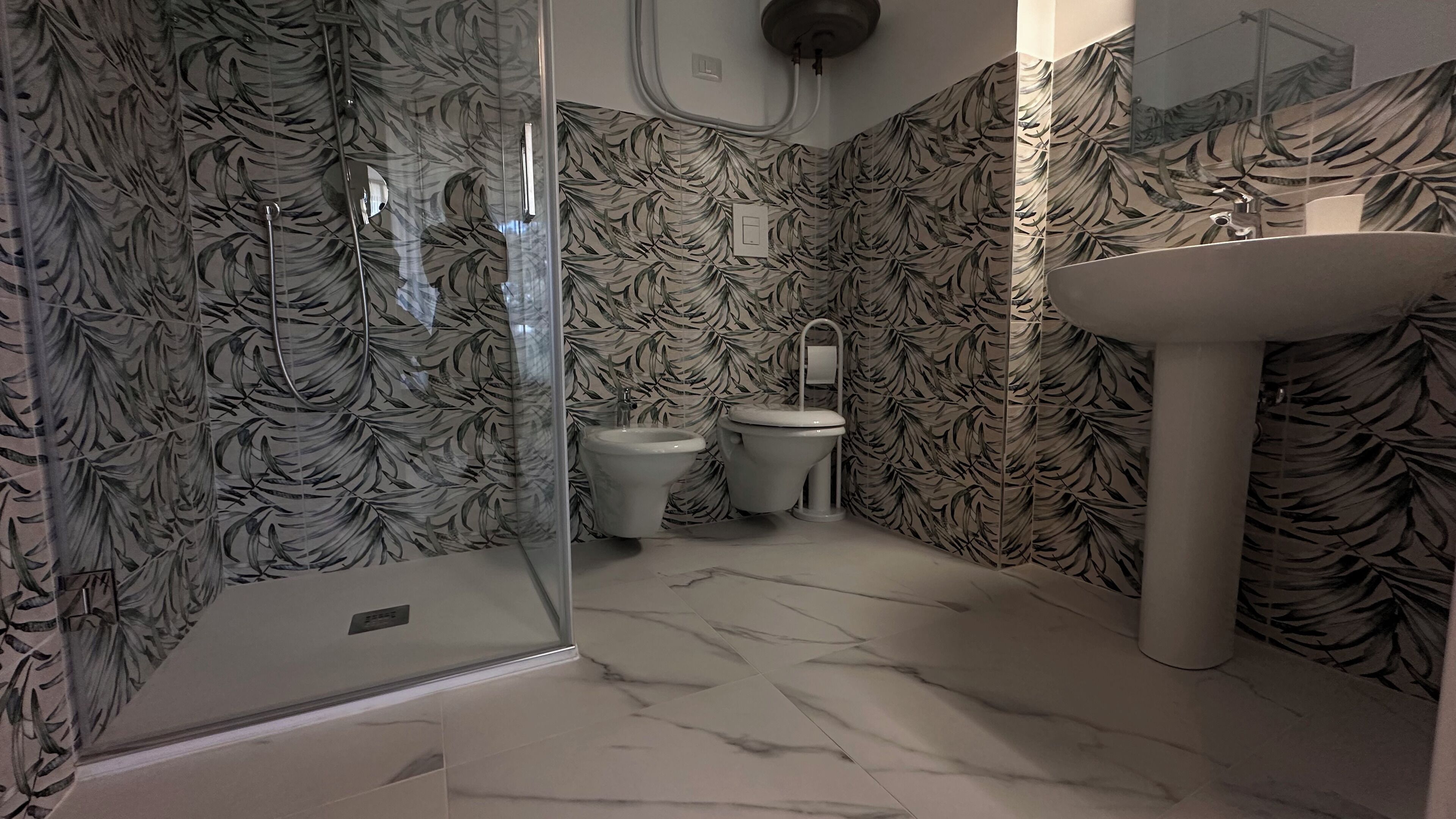 A bathroom with a shower, toilet, and sink, all with a leaf-patterned wallpaper.