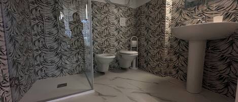 A bathroom with a shower, toilet, and sink, all with a leaf-patterned wallpaper.