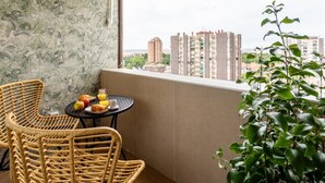 A balcony with wicker chairs, a small round table with breakfast items, and a view of tall buildings.