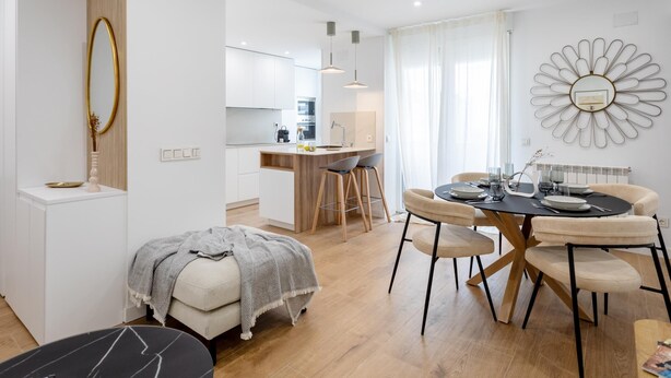 A modern, well-lit apartment with a dining area, kitchenette, and a large mirror.