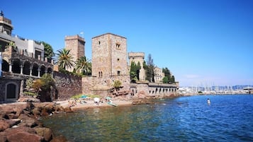 Un bâtiment historique en pierre, doté d’une tour, situé au bord d’une mer d’un bleu limpide.