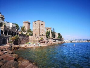 Un edificio de piedra histórico con una torre, situado junto a un mar azul y transparente.