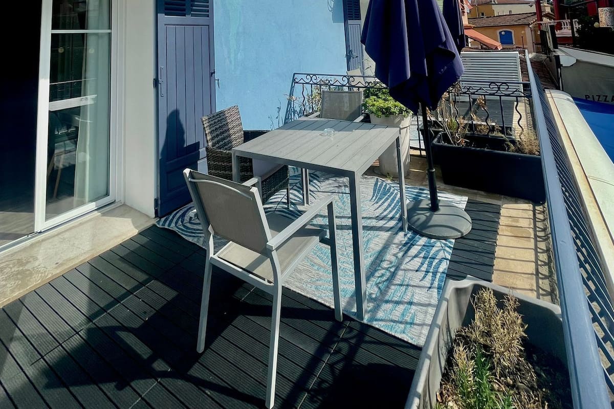 A blue building with a balcony, a table and chairs, and a pool.