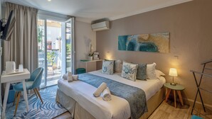 Een hotelkamer met een bed, een bureau, een stoel, een klein tafeltje, een lamp en een schilderij aan de muur.