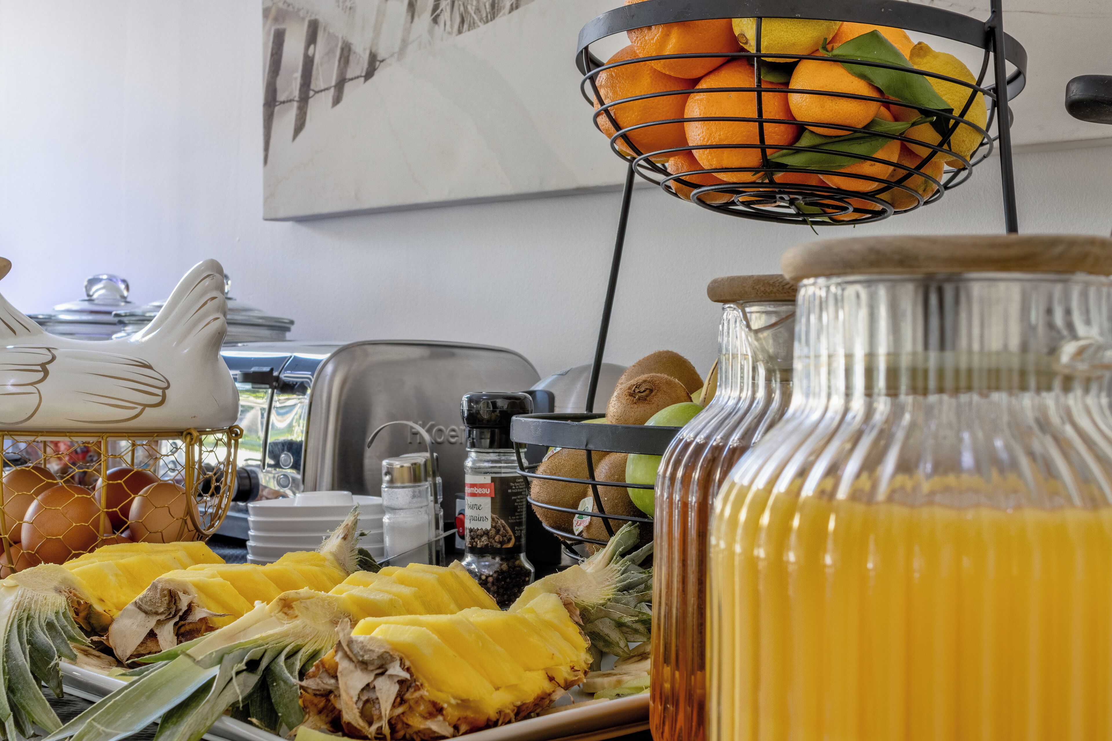 Um buffet de café da manhã com diversas frutas, uma abacaxi e um pote de vidro com suco de laranja.