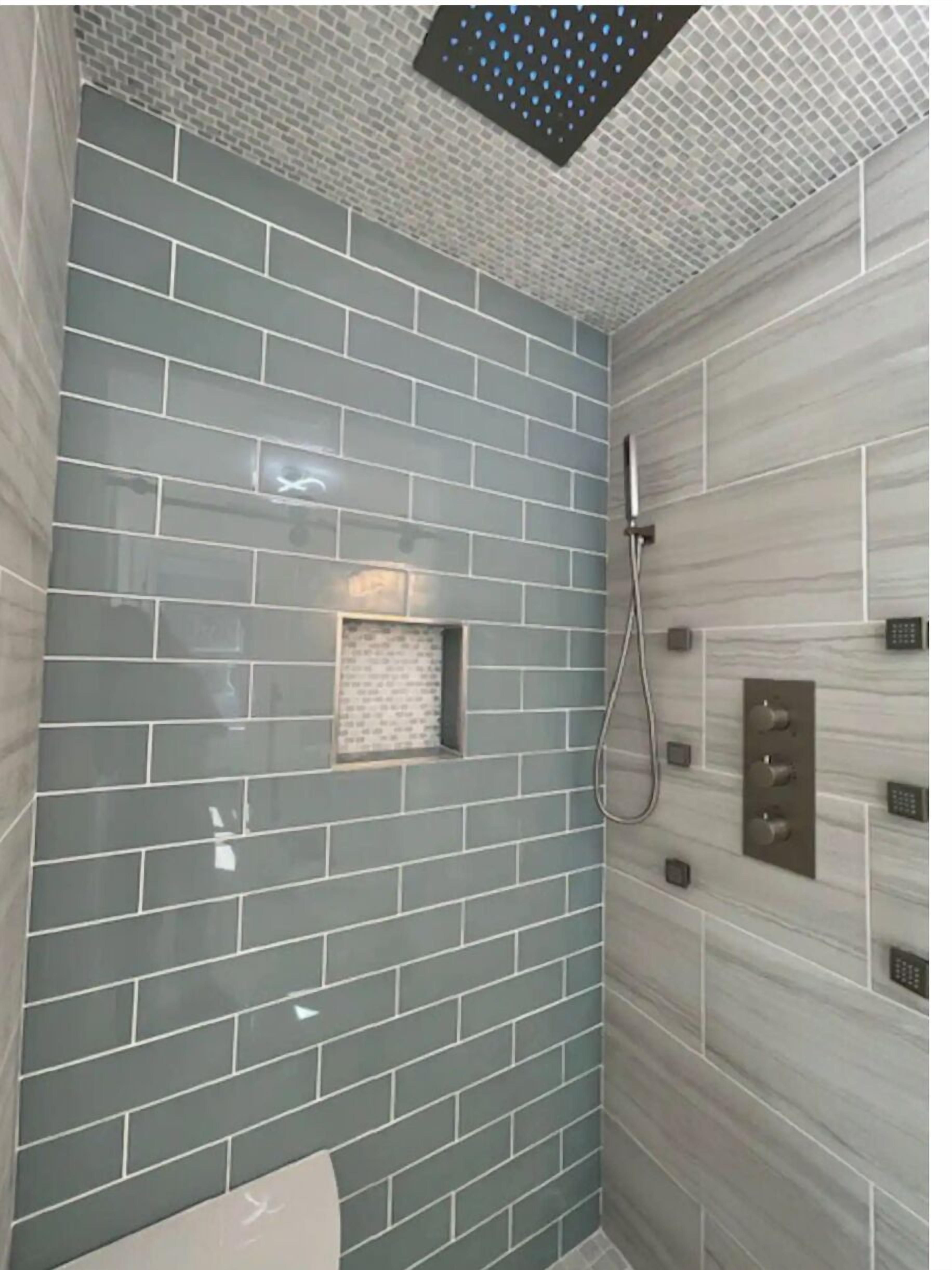 Une salle de bain avec des murs carrelés en bleu et en gris, un espace douche et une petite fenêtre.