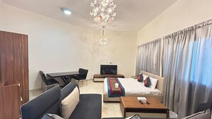 Habitación de hotel con sofá, cama con manta y almohadas, televisor, escritorio con silla y candelabro.