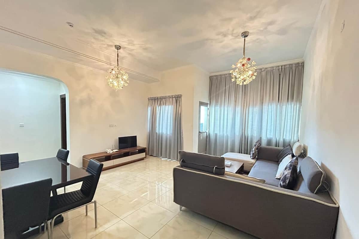 A modern living room with a dining area, two chandeliers, and a large window with curtains.
