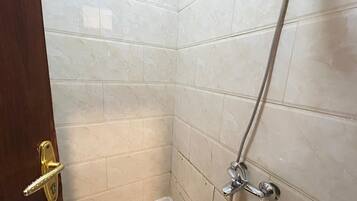 A bathroom with white marble tiles, a shower with a handheld showerhead, and a toilet.