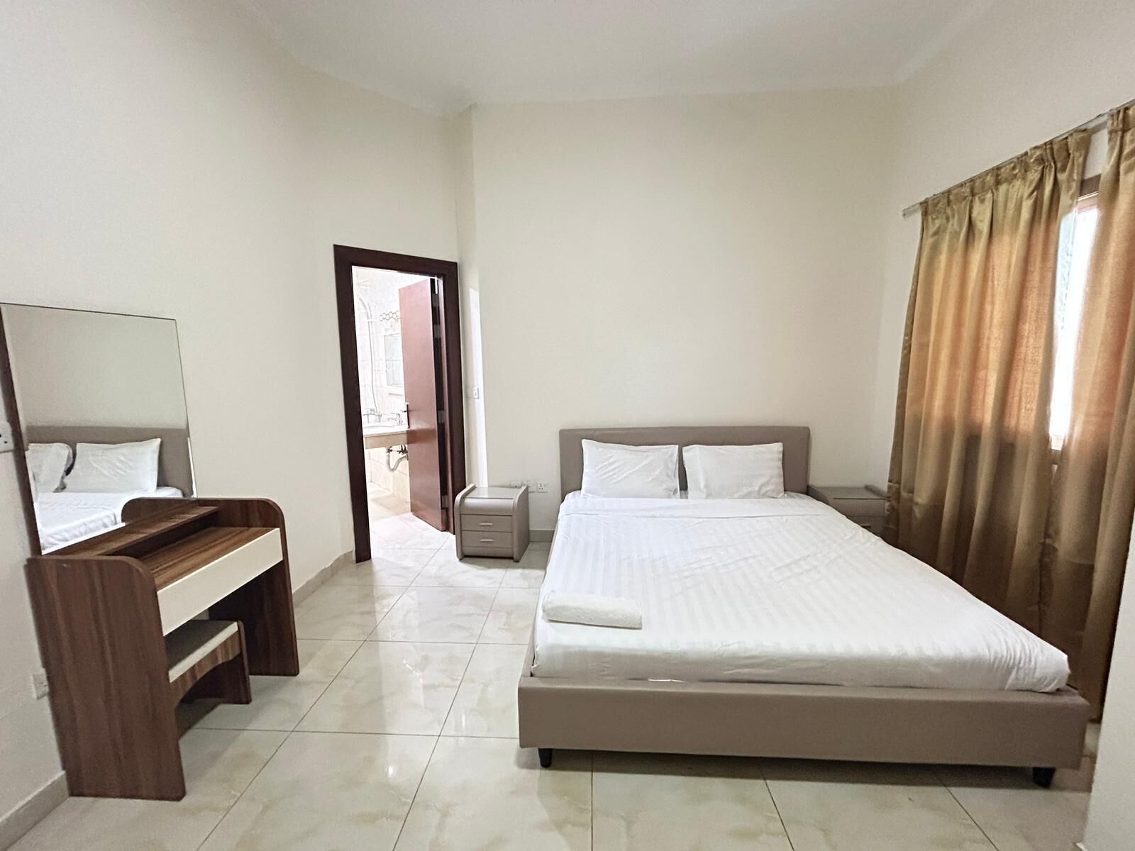 A hotel room with a bed, a desk, a mirror, and a bathroom visible through an open door.