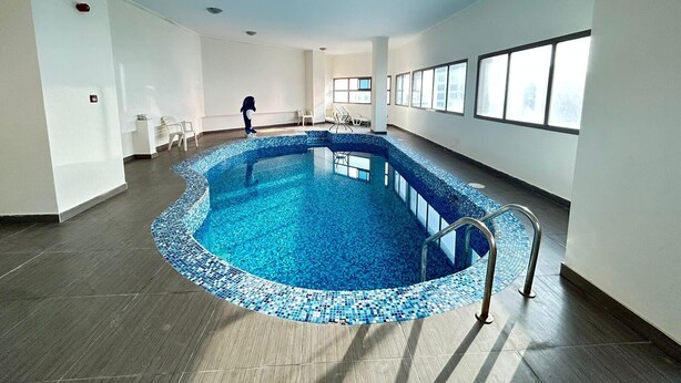 Una piscina interior con borde de azulejos, rodeada de paredes blancas y amplias ventanas.