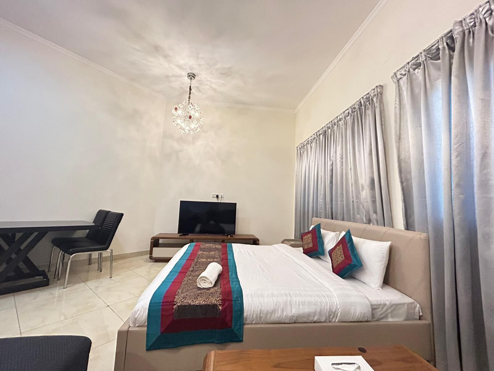Une chambre d’hôtel avec un lit, un bureau, une télévision et un lustre.