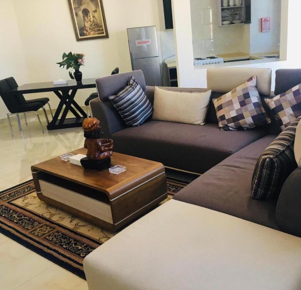A living room with a sofa, a coffee table, and a dining area with chairs and a refrigerator.