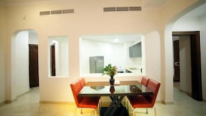 Un comedor con una mesa de vidrio y sillas rojas, una planta en maceta y vista a una cocina con armarios y un refrigerador.