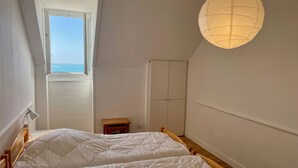 A bedroom with two beds, a window with a view, a hanging light fixture, and a small wooden stool. - "les Yeux en Bleu"- 2 ch- Magnifique vue sur la Grande Plage (Quiberon)