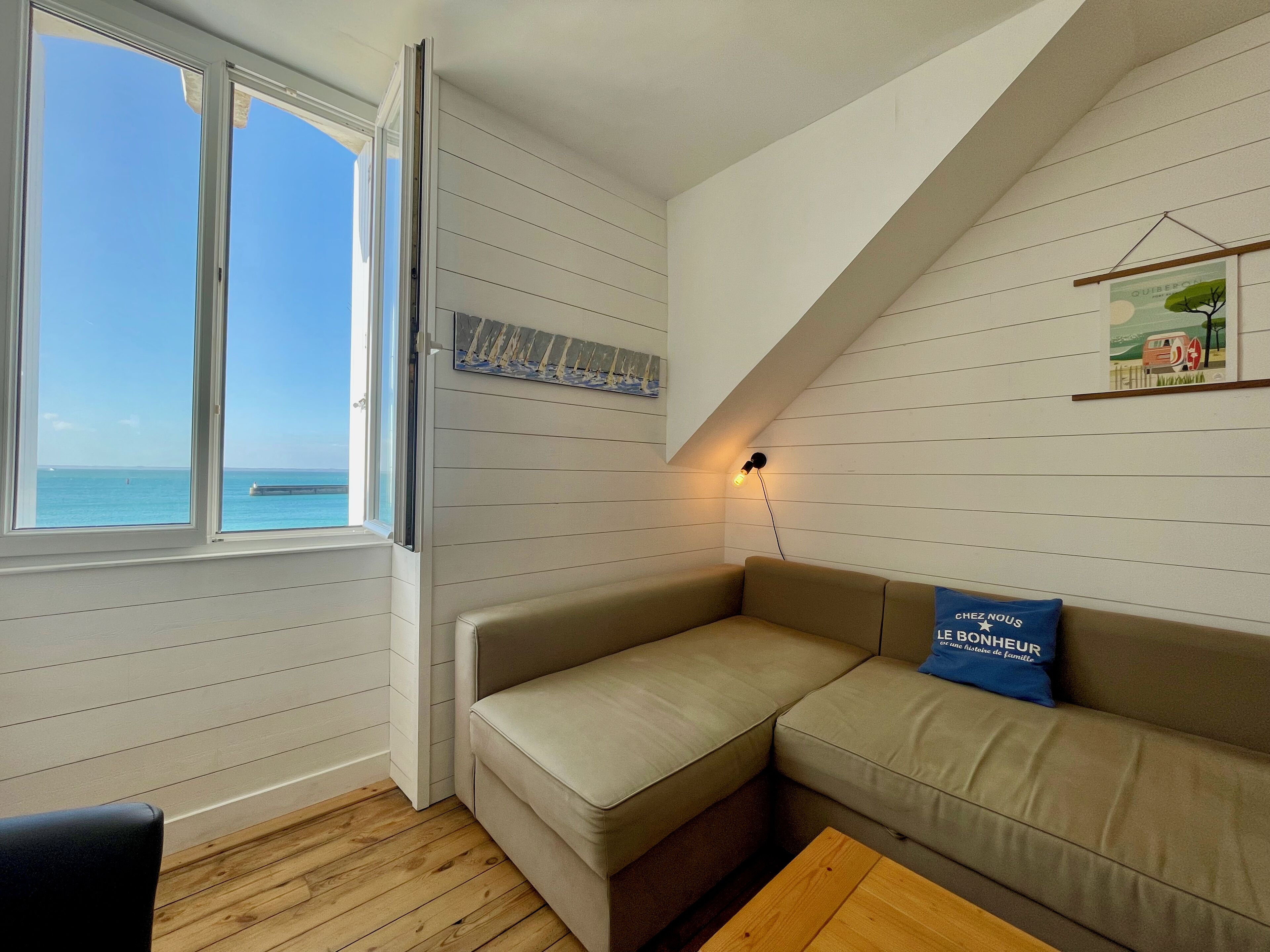 A cozy room with a large window overlooking the sea, a cushioned bench, and a small table.
