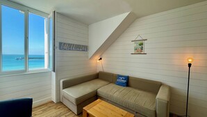 A cozy room with a large window overlooking the sea, a beige sofa, a wooden coffee table, and a floor lamp. - "les Yeux en Bleu"- 2 ch- Magnifique vue sur la Grande Plage (Quiberon)