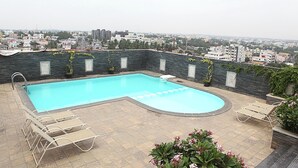Una piscina en la azotea con vistas a la ciudad, rodeada de sillones de descanso y plantas en macetas.
