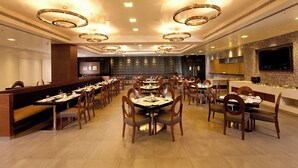 Un restaurante amplio con varias mesas y cabinas, luminarias modernas y un televisor de pantalla plana grande en la pared.
