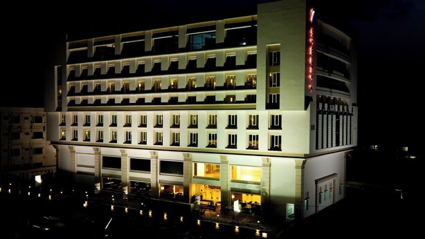 Un hotel de varios pisos con un diseño moderno, que destaca por su entrada principal e iluminación en la fachada.