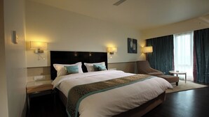 Una habitación de hotel con una cama grande, una silla, una mesita y un ventilador de techo.