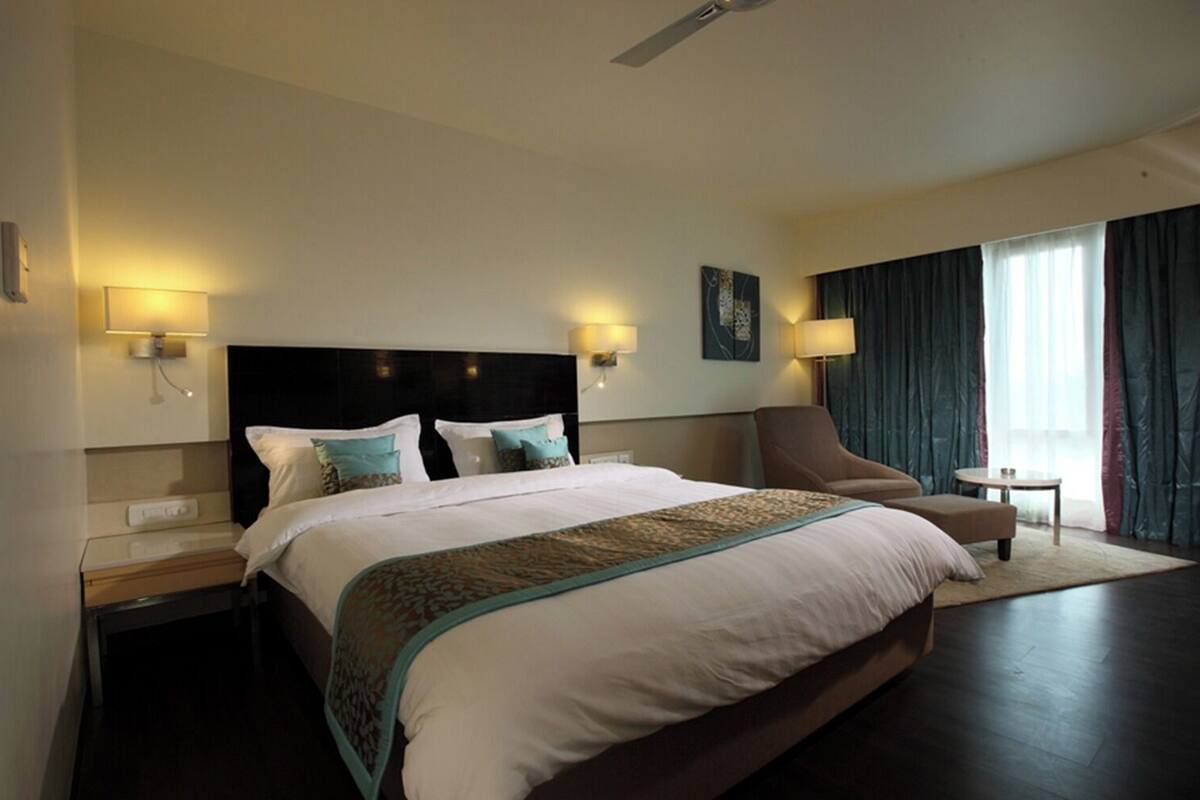 A hotel room with a large bed, a chair, a small table, and a ceiling fan.