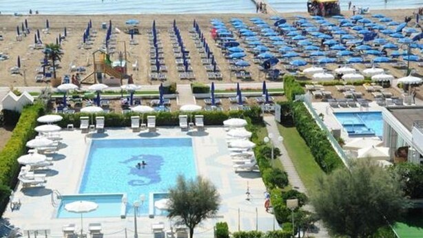 A resort with a swimming pool, beach umbrellas, and a view of the sea. - Hotel Reno (Jesolo)