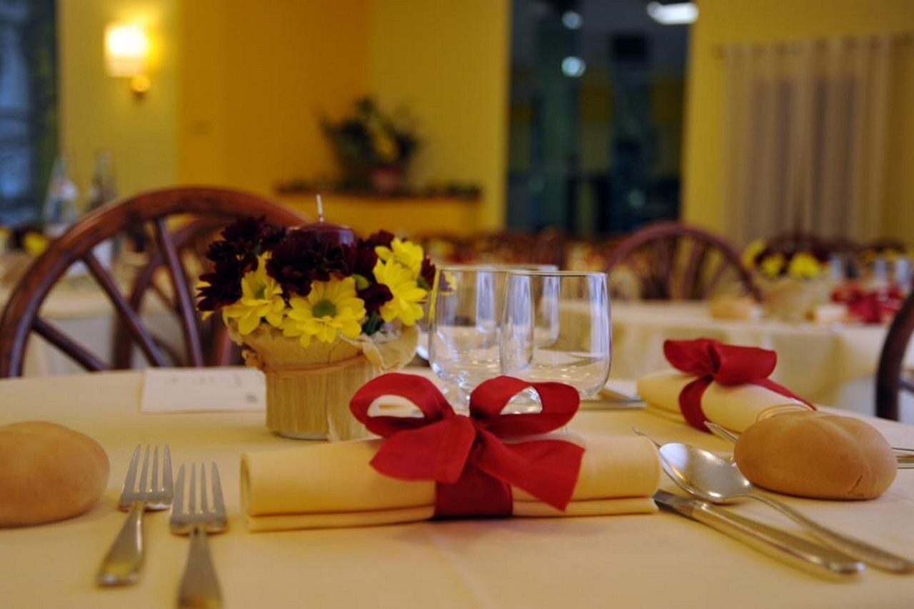 Una tavola imbandita con un vaso di fiori, un bicchiere, posate e un tovagliolo legato con un nastro rosso.
