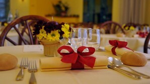A dining table set with a vase of flowers, a glass, cutlery, and a napkin tied with a red ribbon. - Hotel Reno (Jesolo)