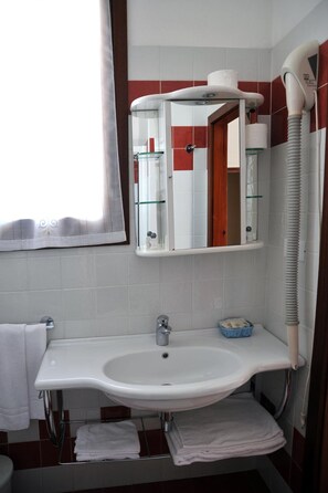 A bathroom with a white sink, a mirror, a towel rack, and a hairdryer. - Hotel Reno (Jesolo)