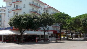 A multi-story hotel with balconies, a restaurant on the ground floor, and a clear sky. - Hotel Reno (Jesolo)