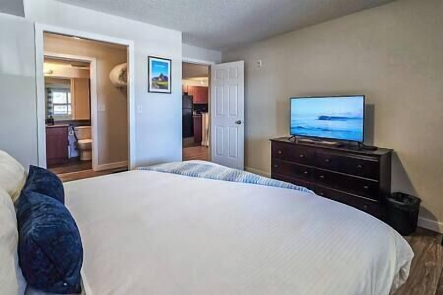 Un dormitorio con una cama grande, un aparador y un televisor que muestra un paisaje.
