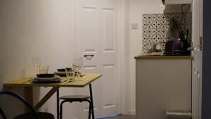 A small dining area with a table set for two, a chair, and a kitchen counter with appliances.