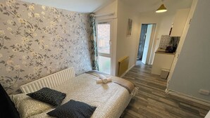 A bedroom with a bed, a radiator, a window, and a view of a hallway.