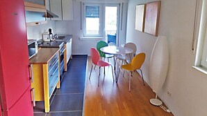 Una cocina compacta con electrodomésticos modernos, una zona de comedor con sillas coloridas y un ventanal que proporciona luz natural.