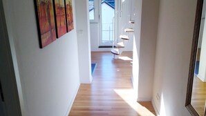 Un pasillo con piso de madera, una escalera y una puerta que da a un balcón.
