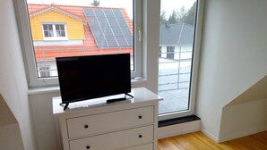 Una habitación con un aparador blanco, un televisor encima y vistas a una casa con paneles solares a través de una ventana.