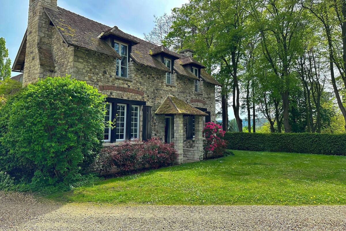 Uma casa de pedra com telhado inclinado, várias janelas e um gramado bem cuidado.
