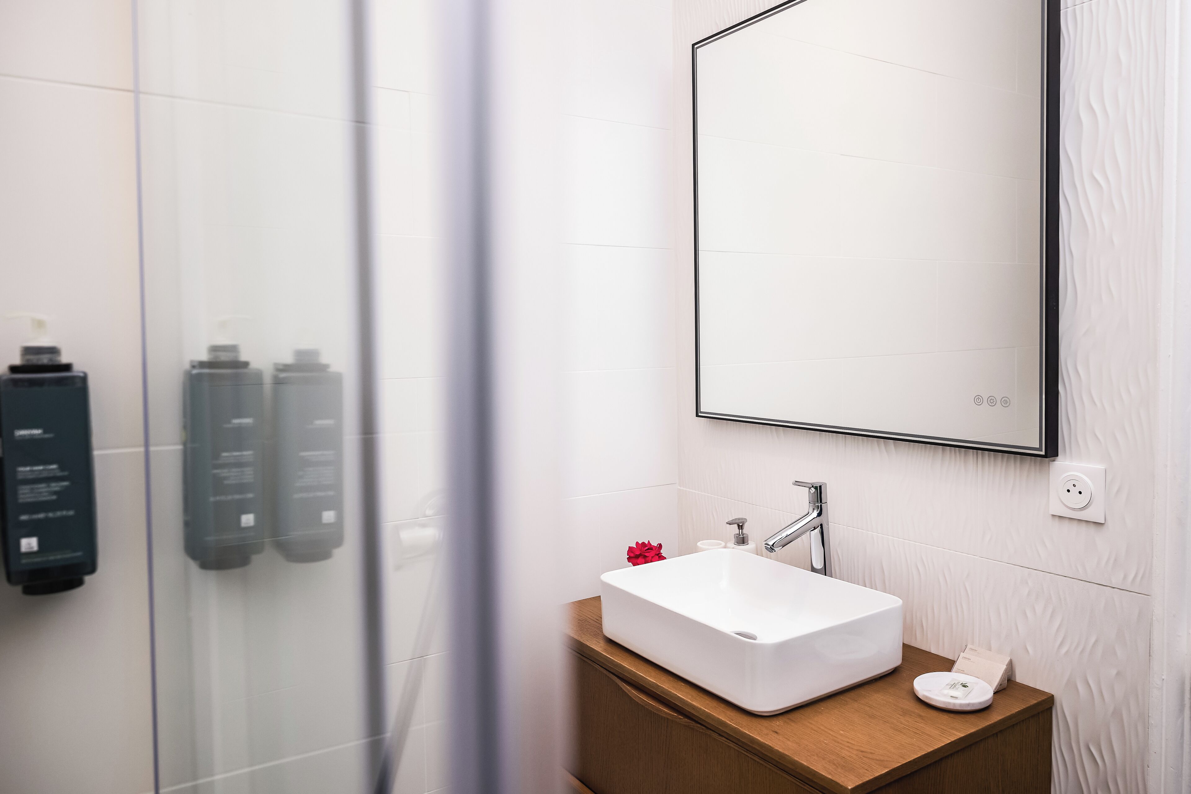 A bathroom with a white sink, wooden vanity, and a large mirror.