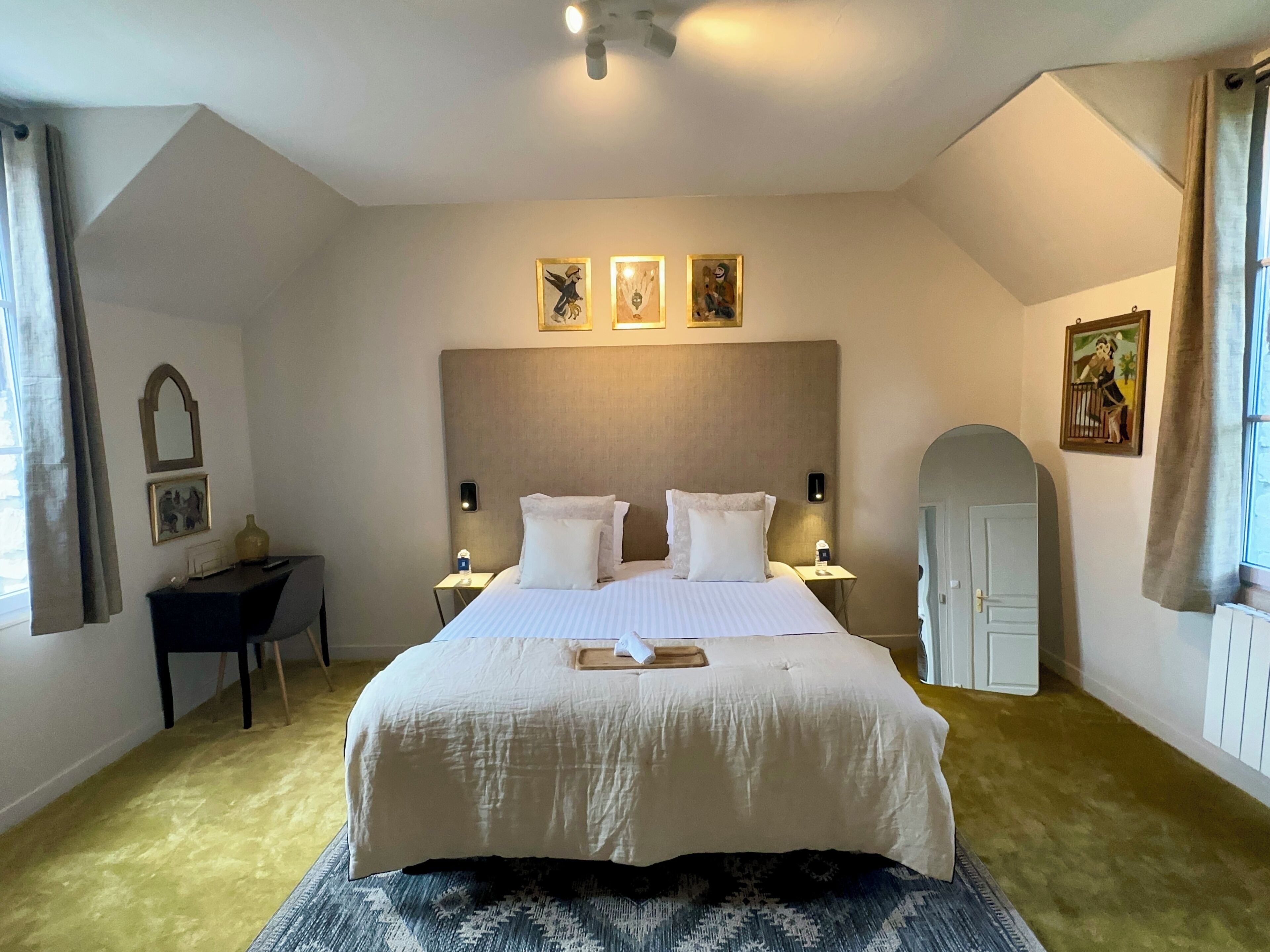 A hotel room with a large bed, a desk, a chair, a small table, and a door.
