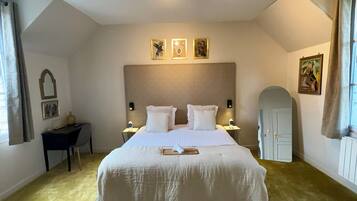 A hotel room with a large bed, a desk, a chair, a small table, and a door.