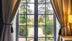 Um quarto com uma janela grande, cortinas, uma mesa e uma cadeira.